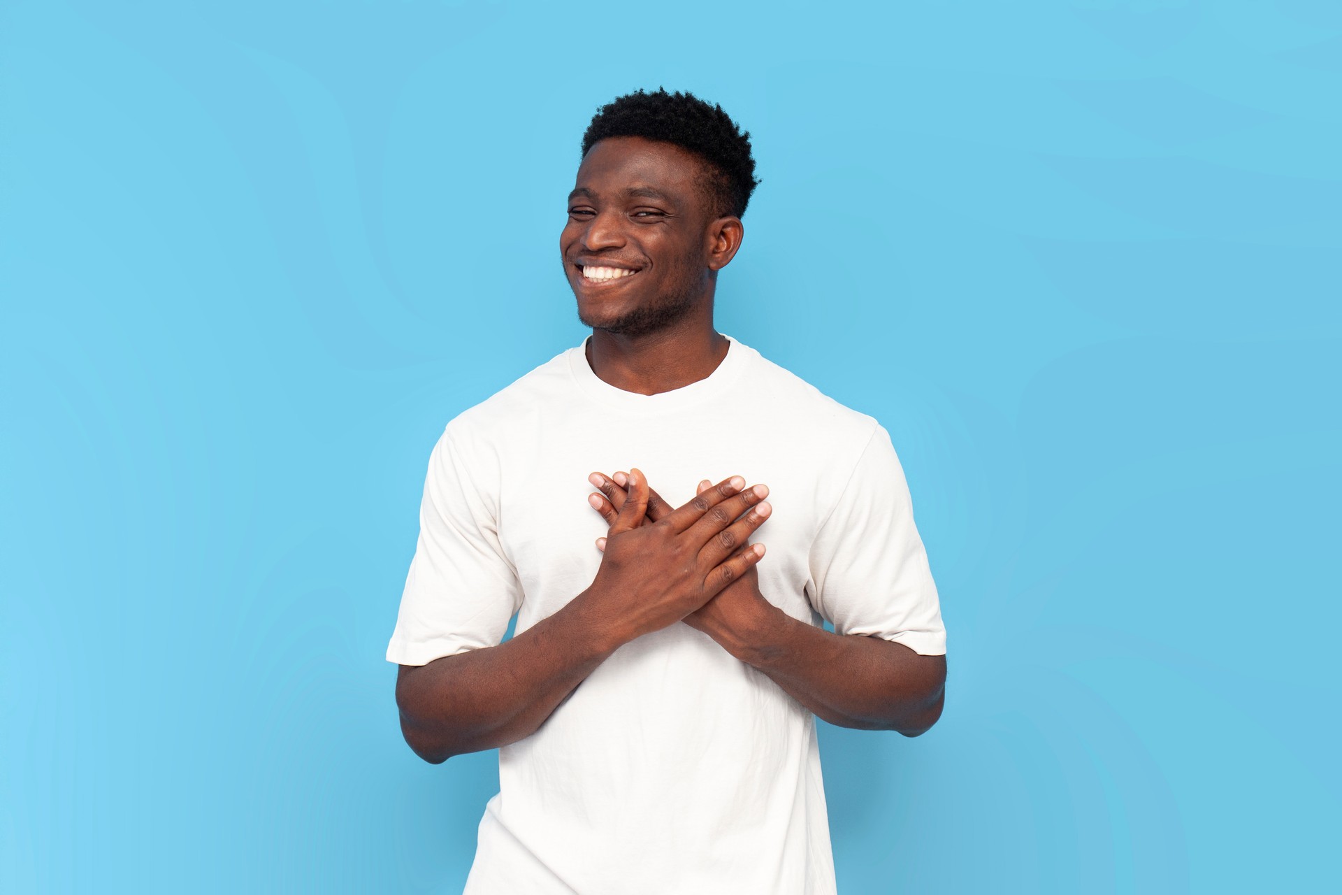 gratitude gesture. african american man in white t-shirt holds his hands on his heart and smiles